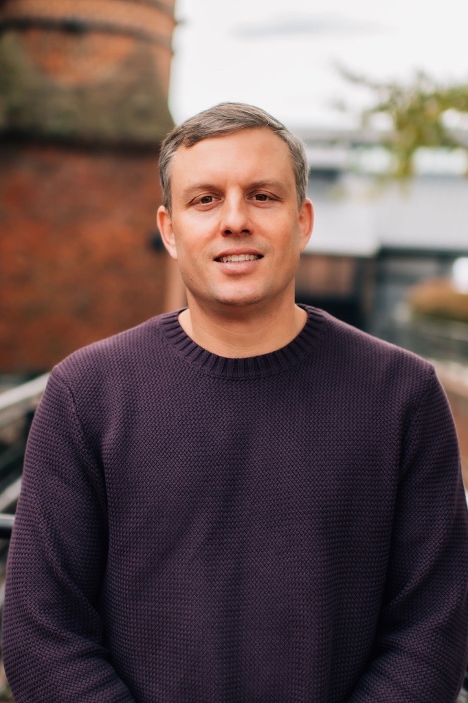 Man in purple sweater, outdoor background.